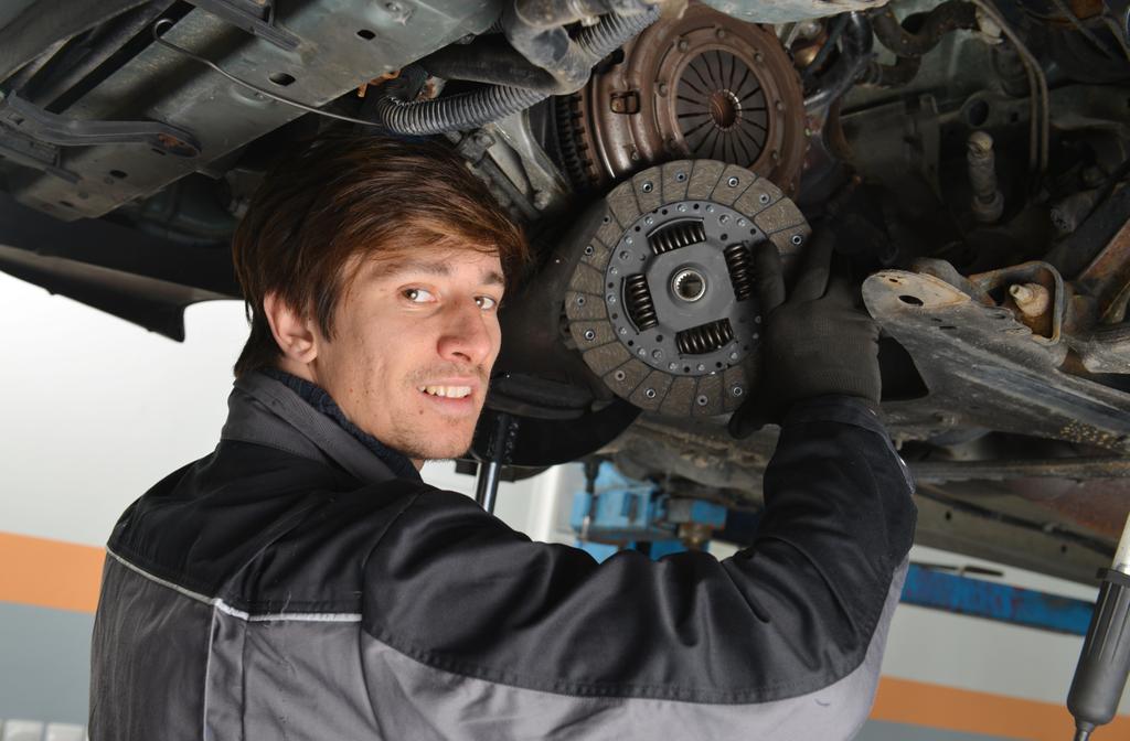auto mechanic working under the car and changing clutch at car repair shop
